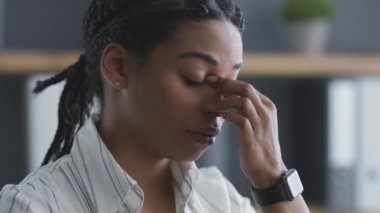 Aşırı çalışma konsepti. Yorgun Afrikalı Amerikalı kadın baş ağrısından muzdarip, ofisteki burun köprüsünü ovuyor, ağır çekimde