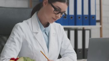 Gözlüklü genç, profesyonel doktor beslenme uzmanı. Tıbbi formda tedavi planı yazıyor, ofisinde çalışıyor.