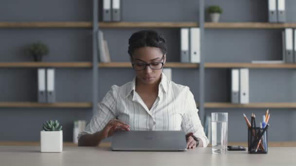 Burnout profesional. Joven mujer afroamericana cansada en gafas cerrando laptop y sentada en el lugar de trabajo — Vídeos de Stock