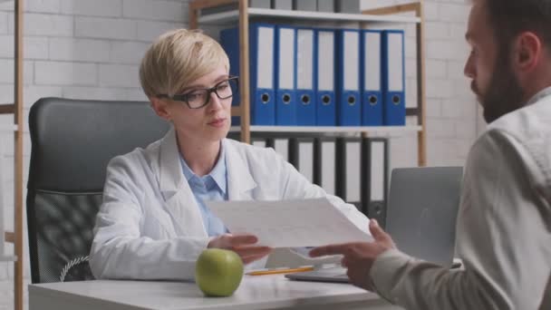 Cuidado médico mujer de mediana edad dando recetas a paciente masculino, hablando durante la consulta personal en la clínica — Vídeo de stock