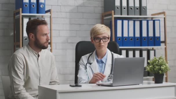 Média idade médico consulta paciente masculino no escritório, mostrando resultados de pesquisa no computador portátil — Vídeo de Stock