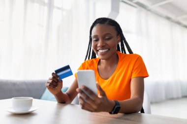 Yeni online alışveriş uygulaması. Neşeli siyah kadın cep telefonu ve kredi kartı kullanıyor, web mağazasından mal alıyor.