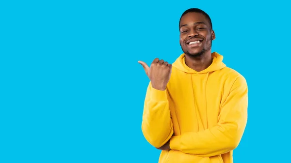 Sonriente africano chico señalando dedo pulgar a un lado sobre fondo azul —  Fotos de Stock