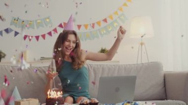 İyi tatiller. Genç bayan doğum gününü arkadaşlarıyla internetten kutluyor, şampanya içiyor ve konfeti altında dans ediyor.