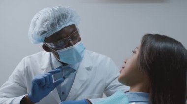 Profesyonel siyahi dişçi kadın hastayla konuşuyor, diş sağlığı kliniğinde tedavi öncesi tedavi planını anlatıyor.