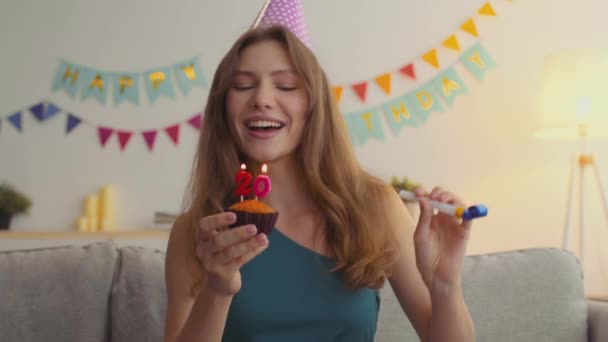 Jovem alegre em boné de aniversário soprando velas em cupcake e dança, comemorando com amigos on-line — Vídeo de Stock