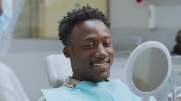 Feliz joven afroamericano chico paciente mirando al espejo y sonriendo, disfrutando del resultado del tratamiento, cámara lenta — Vídeos de Stock