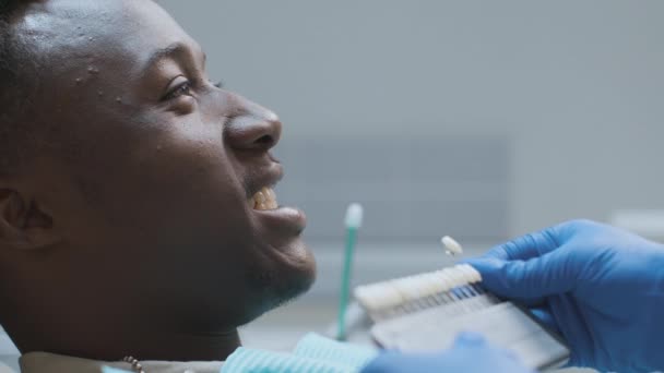 Fogskála mintákat alkalmazó fogorvos mosolygó fekete férfi páciensnek a fogászati klinikán, közeli portré, lassított felvétel — Stock videók