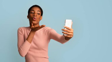 Genç, güzel, Afro-Amerikalı bir kadın akıllı telefondan selfie çekerken öpüşüyor.