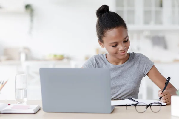 Feliz adolescente ocupado afro-americano menina estudando à mesa com laptop, no interior da cozinha — Fotografia de Stock