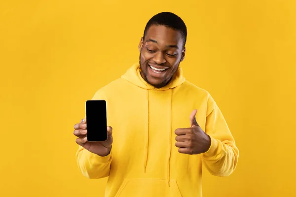 Africano americano cara mostrando celular tela gesturing polegares para cima, fundo amarelo — Fotografia de Stock