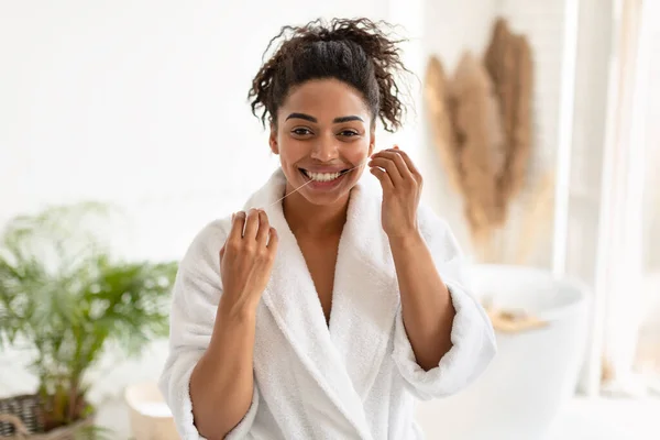 Feliz preto mulher fio dental dentes sorrindo para câmera no banheiro — Fotografia de Stock