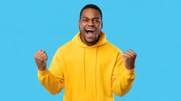 Emotionaler afroamerikanischer Typ, der mit den Fäusten über den blauen Hintergrund brüllt — Stockfoto