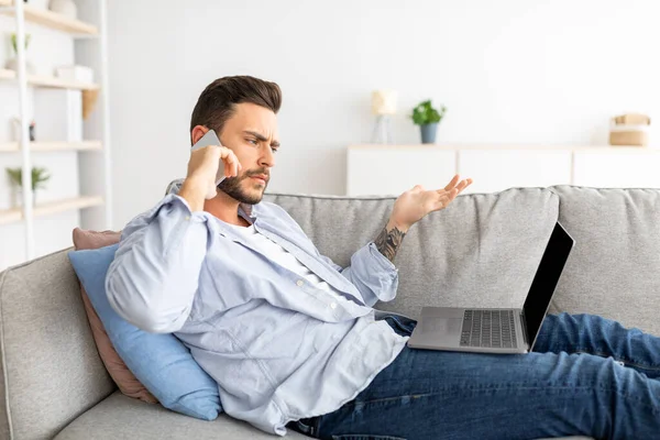 Tipo emocional que sufre problemas con el ordenador portátil, llamando a atención al cliente mientras está sentado en el sofá en casa, espacio libre — Foto de Stock