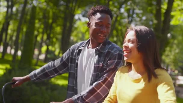 Aktywny wypoczynek. Młoda, szczęśliwa afrykańska para zakochana w sobie spacerując razem z rowerami w parku publicznym — Wideo stockowe