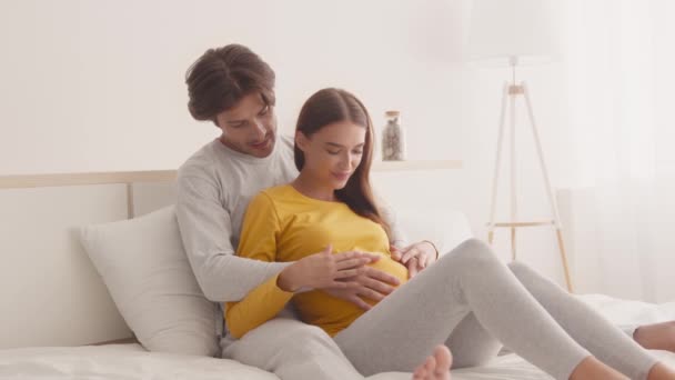 Giovane uomo e donna incinta che si abbracciano insieme sul letto, accarezzando grande pancia, godendo di un periodo di pace della gravidanza — Video Stock