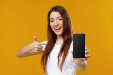 Neşeli güzel bayan boş ekranla cep telefonunu işaret ediyor.