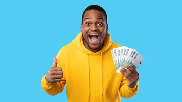 Espited Black Guy Holding Euro Money Gearuring Thumbs-Up, Blue Background — 스톡 사진