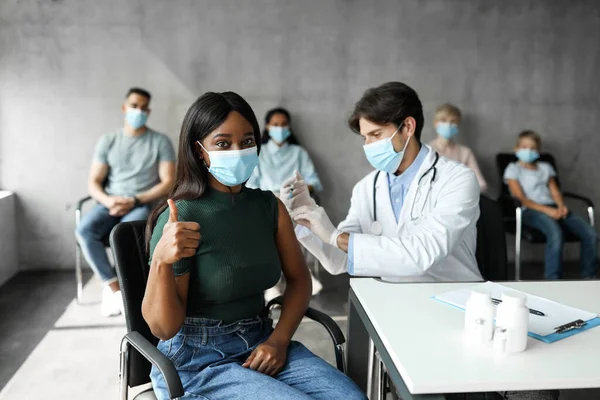 Joven dama negra en mascarilla recibiendo la vacuna en la clínica —  Fotos de Stock
