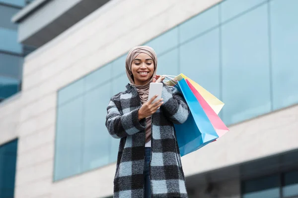 Посмішка досить африканського американця жінка в хіджабі і пальто з пакетами закупівель насолоджуються покупками — стокове фото