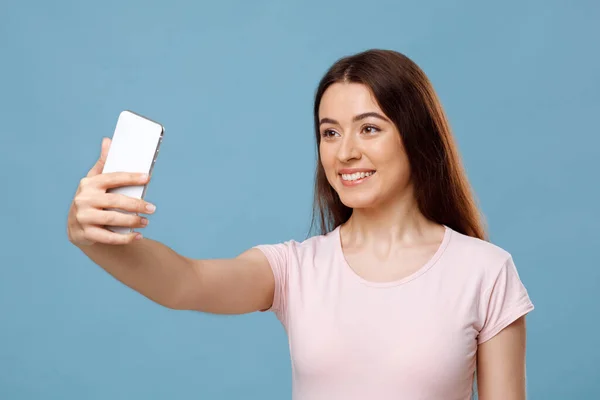 Çekici genç bayan mavi stüdyo arka planında selfie çekiyor. — Stok fotoğraf