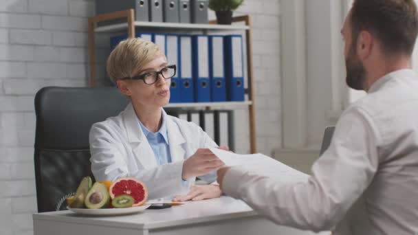 Personlig näringsplan. Professionell kvinna dietist ger papper till patienten, talar om kost under konsultation — Stockvideo