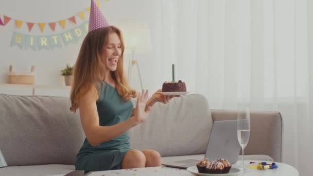 Saudação online. Jovem senhora em vídeo cap festa chamando a amigo, segurando bolo com fogo de artifício e cantando feliz aniversário — Vídeo de Stock