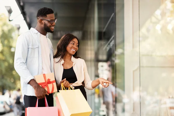 Retrato de casal negro com sacos de compras apontando para a janela — Fotografia de Stock