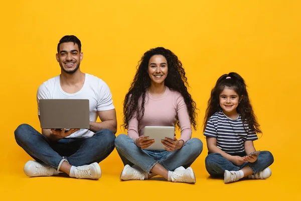 Tecnologie per la famiglia. Arabo mamma, papà e figlia seduta con diversi gadget — Foto Stock