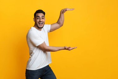 Şaşırmış Orta Doğulu adam sarı üzerinde görünmez bir şey tutuyor.