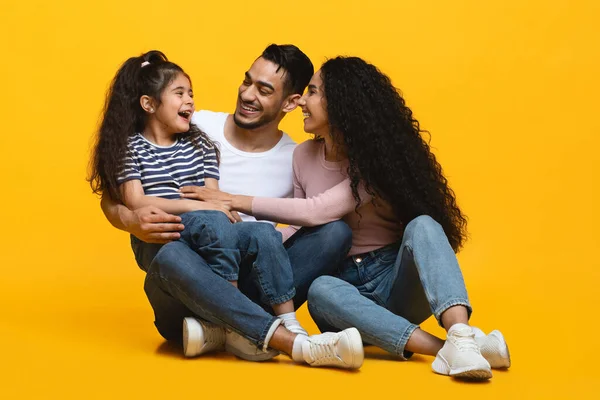 Alegres pais árabes se divertindo com a pequena filha sobre fundo estúdio amarelo — Fotografia de Stock