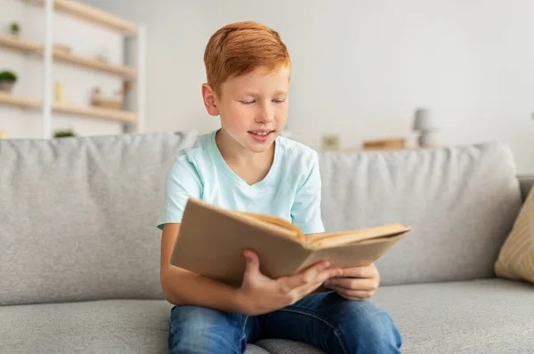 Симпатичный рыжий мальчик сидит дома и читает книгу. — стоковое фото