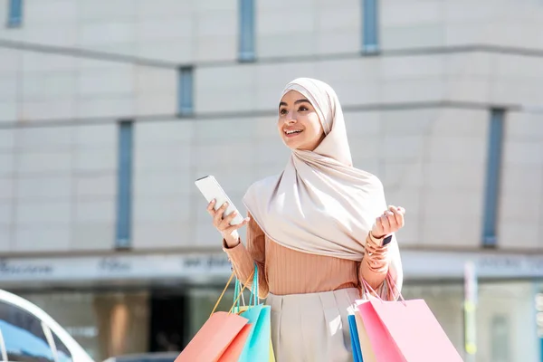 Şaşırtıcı bir şekilde tesettürlü, tesettürlü, güzel, genç bir Arap kadın, bir sürü paketle, telefonla mesaj yolluyor. — Stok fotoğraf