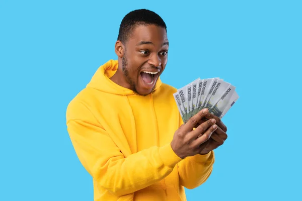 Радостный афроамериканец кричит, держа в руках евро-деньги, голубой фон — стоковое фото