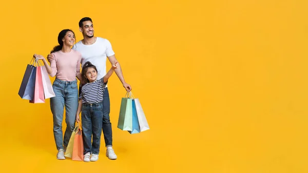 Oferta de compras. Familia Árabe De Tres Llevando Bolsas De Comprador Y Señalando Fuera —  Fotos de Stock