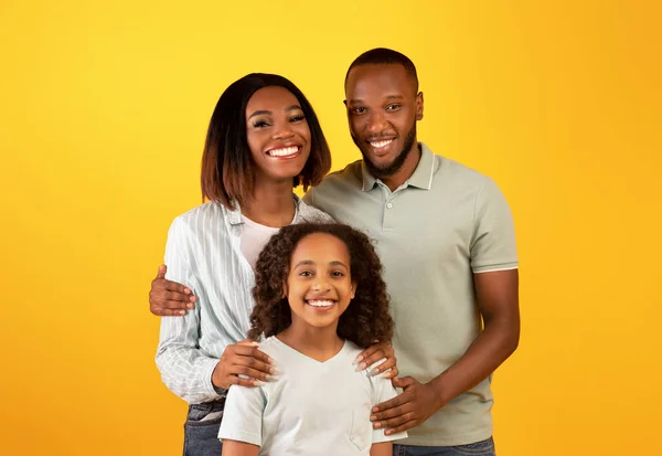 Familie liefde concept. Portret van zwart gezin met dochter knuffelen en glimlachen op camera staan op gele achtergrond — Stockfoto