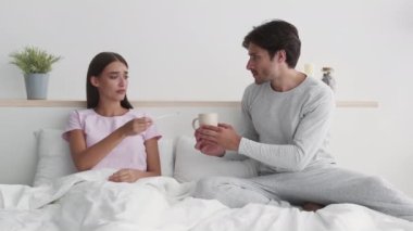 Genç ve endişeli koca hasta karısına çay getiriyor ve onu destekliyor. Ateşli kadın yatakta uzanıyor, ağır çekimde.