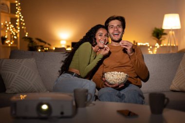 Ev sinema projektörünü kullanarak film izleyen çift içeride gülüyor.