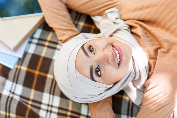 Satisfait heureux jeune femme musulmane arabe dans le hijab reposant dans le parc, se trouve sur plaid dans le jardin universitaire — Photo