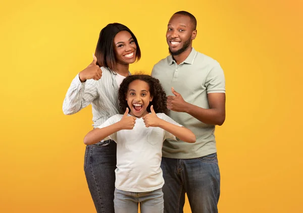 Beste aanbod voor gezinnen. opgewonden afrikaanse amerikaanse ouders en hun dochter tonen duimen omhoog over gele achtergrond — Stockfoto
