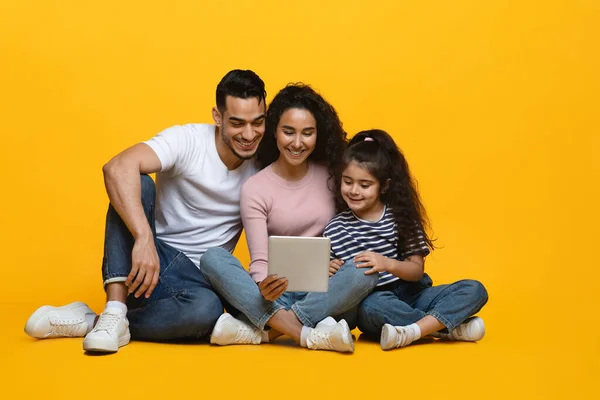 Happy Middle-Eastern Family Of Three With Digital Tablet On Yellow Studio Background — Stock Photo, Image
