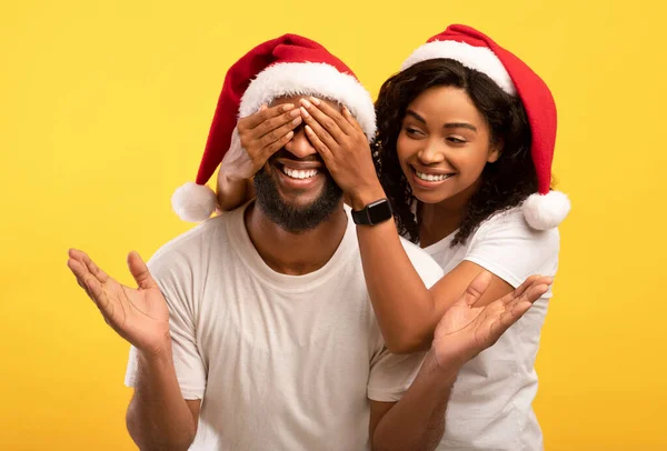 Hadiah terbaik untuk Natal. Happy african american lady berdiri di belakang laki-laki dan menutup matanya, latar belakang studio kuning — Stok Foto