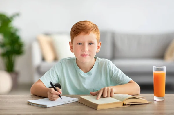 Liebenswerter Rotschopf liest Buch und schreibt Notizen — Stockfoto