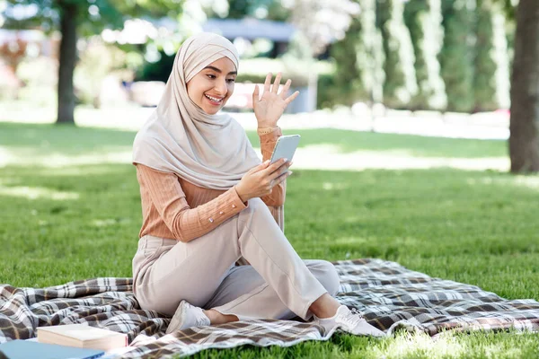 Boldog fiatal arab muszlim nő hidzsáb hívások okostelefon, videó találkozó a zöld parkban — Stock Fotó