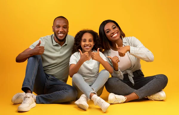 3人のアフリカ系アメリカ人の家族が親指を立てて何かを推薦し黄色の背景に座って — ストック写真