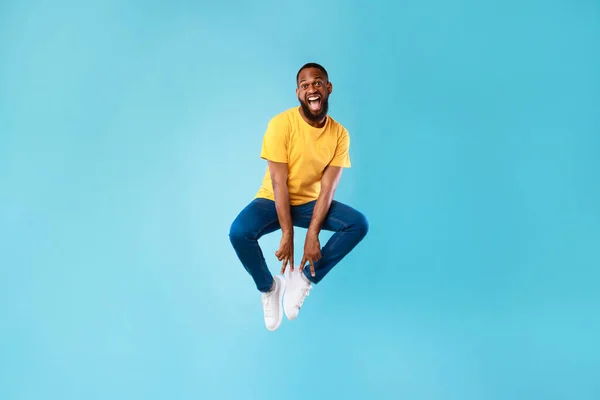 Verrückter afroamerikanischer Typ springt auf und macht Friedensgeste mit beiden Händen auf blauem Studiohintergrund — Stockfoto