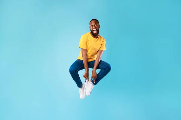 Loco afroamericano saltando y haciendo un gesto de paz con ambas manos en el fondo del estudio azul —  Fotos de Stock