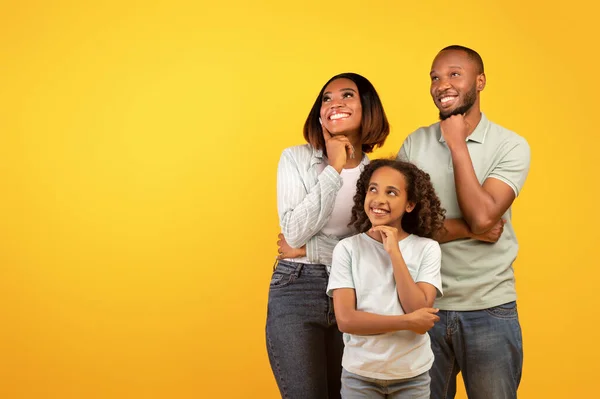 Speciale aanbieding. Jonge zwarte familie van drie kijken opzij op vrije ruimte en hand in hand op kin, gele achtergrond — Stockfoto