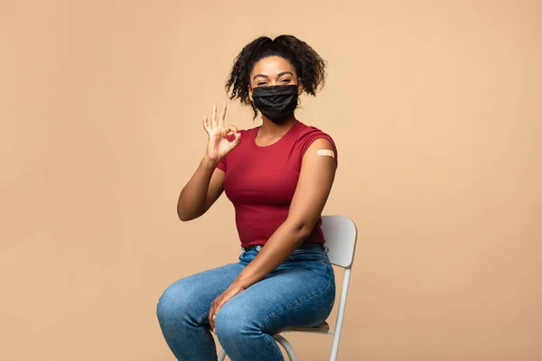 Giovane donna afro in maschera facciale che mostra un gesto corretto dopo l'iniezione del vaccino covid-19, raccomandando l'immunizzazione coronavica — Foto Stock