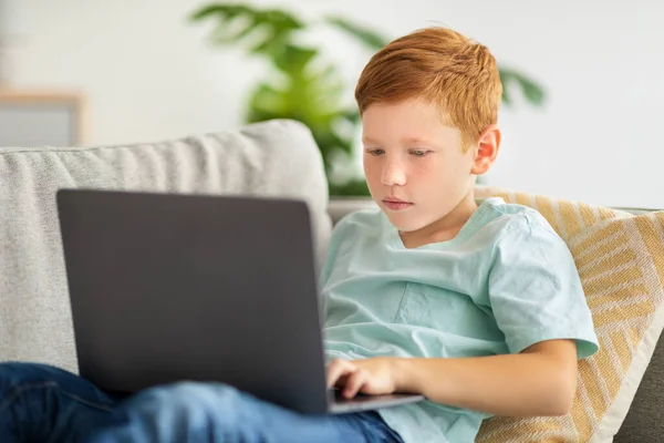 Redhead pojke med hjälp av bärbar dator, spela online TV-spel — Stockfoto